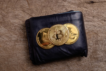 Gold physical Bitcoin, Litecoin and Ethereum coins on black leather wallet, wooden background