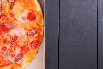 Pizza on a black wooden background, Italian pizza with tomatoes, bacon, sausages and cheese, fast food, festive food on a dark background, copy space, American cuisine