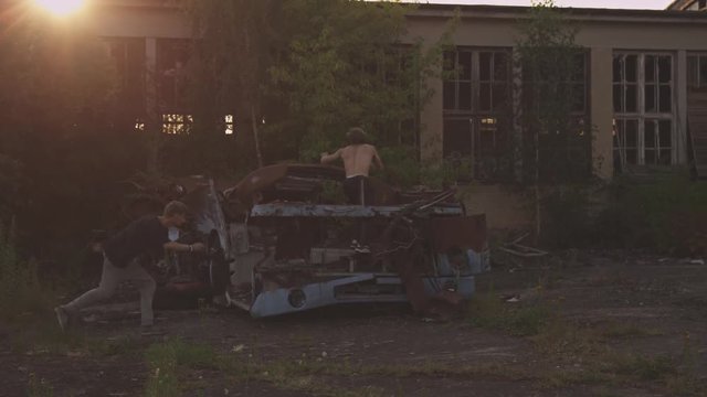 two parkour guys doing a run over an old truck together in the sunset