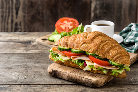 Croissant sandwich with cheese, ham and vegetables on wooden table. Copyspace