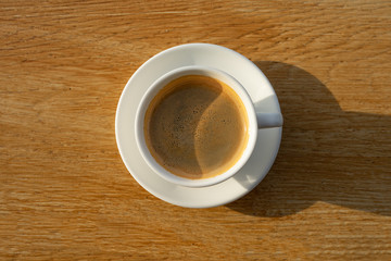 coffee in white cup with sunlight on wood background 