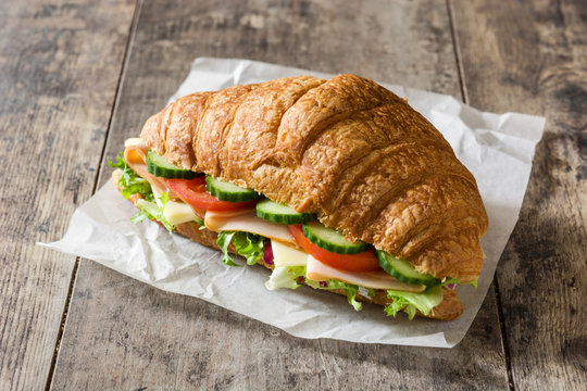 Croissant sandwich with cheese, ham and vegetables on wooden table. 