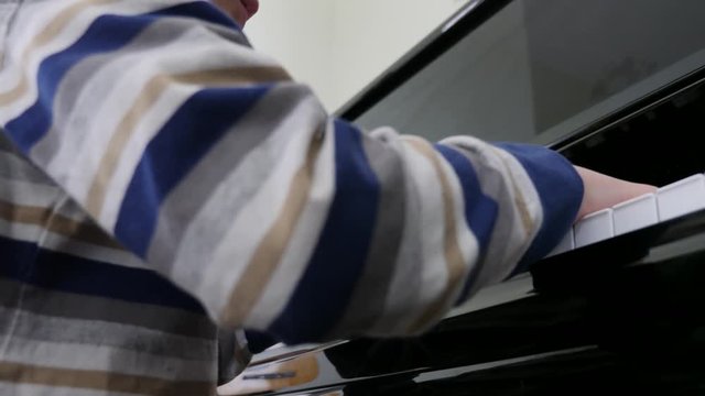 Dolly of cute little boy practicing a black upright piano at home low shot