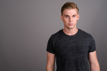 Young handsome man with blond hair wearing gray shirt against gr
