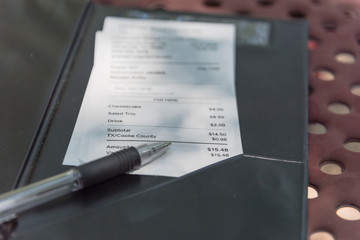 Close-up open leather bill holder with restaurant check and pen. Top view, soft focus receipt with...