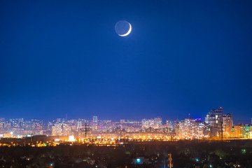 City at night with new moon on dark blue sky with stars