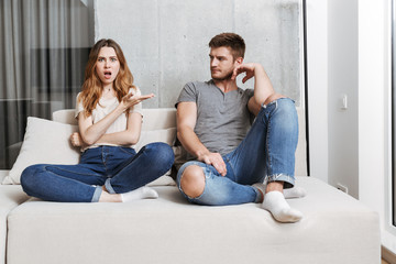 Displeased young loving couple sitting on sofa quarrel.