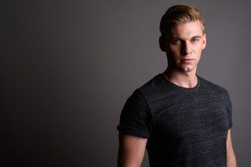 Fototapeta premium Young handsome man with blond hair wearing gray shirt against gr