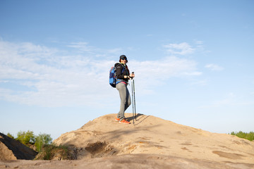 Obraz premium Photo of smiling tourist girl with backpack and walking sticks on hill
