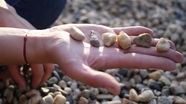 Female lay out sea pebbels on her palm during rest relax on a beach