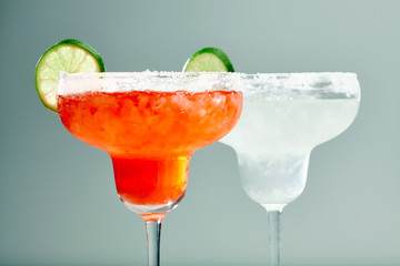 Closeup of two cocktails in wine glasses red and white decorated with lime slices.