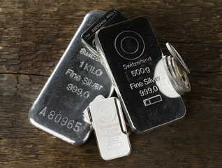 Silver bullion. Cast and minted bars and coins on the background of wood texture.
