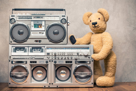 Retro Teddy Bear toy standing near boombox cassette ghetto blasters radio recorders from 80s front concrete wall background. Vintage old style filtered photo