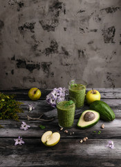 Green fruit smoothie in glasses on wooden background with flowers