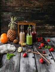 Delicious detox smoothies in glass bottles on rustic wooden board with assorted fruits