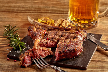Grilled cowboy beef steak, glass of beer, herbs and spices on a wooden background. Top view.