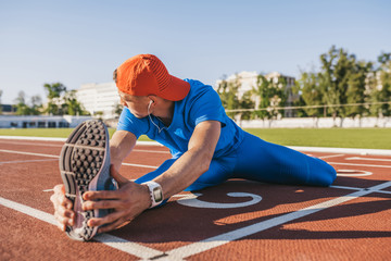 Young athlete male stretching his leg on a track in stadium, preparing for running and jogging...