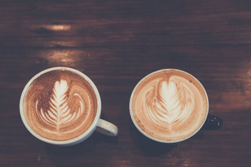 Two Coffee cup with latte art on wooden background . Selective focus white cup.color vintage style