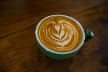 top view of Coffee cup with latte art on wooden table . Selective focus green cup.color vintage style.
