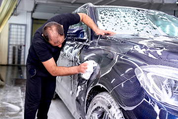 A man washes a blue car. Thorough washing of the body with foam and a high-pressure apparatus