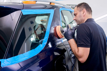 A man is polishing a blue car. Polishing machine and polishing paste for gloss.