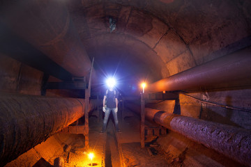 Urban explorer with candle in underground communication, heating main, sewer tunnel, etc. 