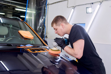 A man is polishing a blue car. Polishing machine and polishing paste for gloss.