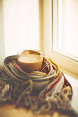 small and big red mug wrapped in a blue scarf and standing on the table against the background of a winter window / warming atmosphere for hanging out