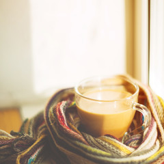small and big red mug wrapped in a blue scarf and standing on the table against the background of a winter window / warming atmosphere for hanging out