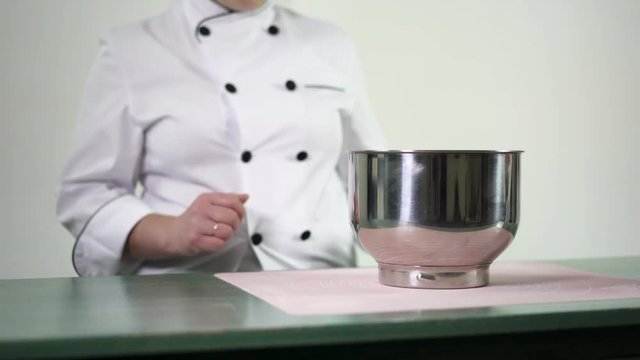 Confectioner preparing great pan for whipping cream. Baker in a uniform putting pot on the tabble for making biscuits cake