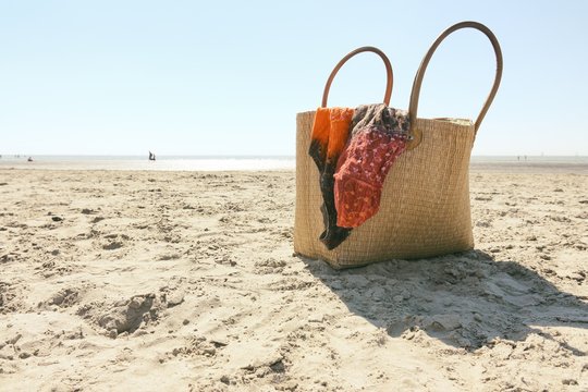 Beach wicker bag on a sandy beach with part of an orange dress against a blue sky