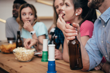 close up view of fan horns on bar counter and group of friends with beer bottles watching soccer match