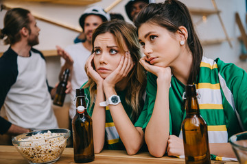 upset young women and their male friends standing behind during watch of soccer match at bar