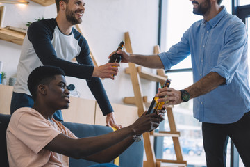 cropped shot of man giving beer bottles to smiling multiethnic friends at home