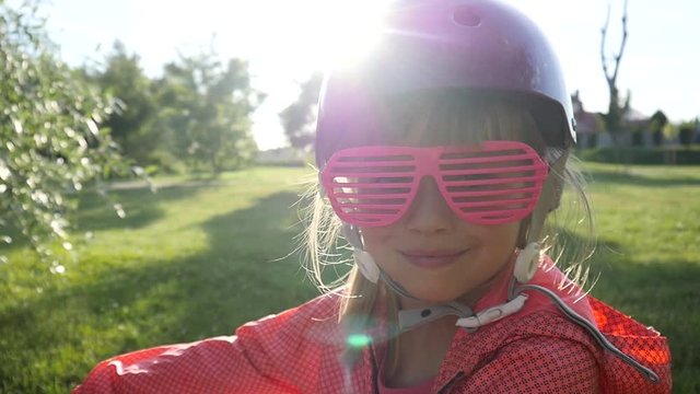 Cute little kid girl smily face portrait on a bicycle in a green park in sunset sun rays