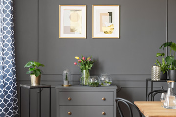 Flowers on grey cabinet under posters in minimal loft interior with plants. Real photo