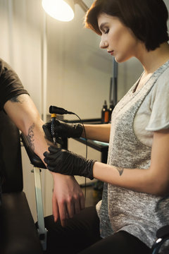 Young woman tattooist doing tattoo on male arm