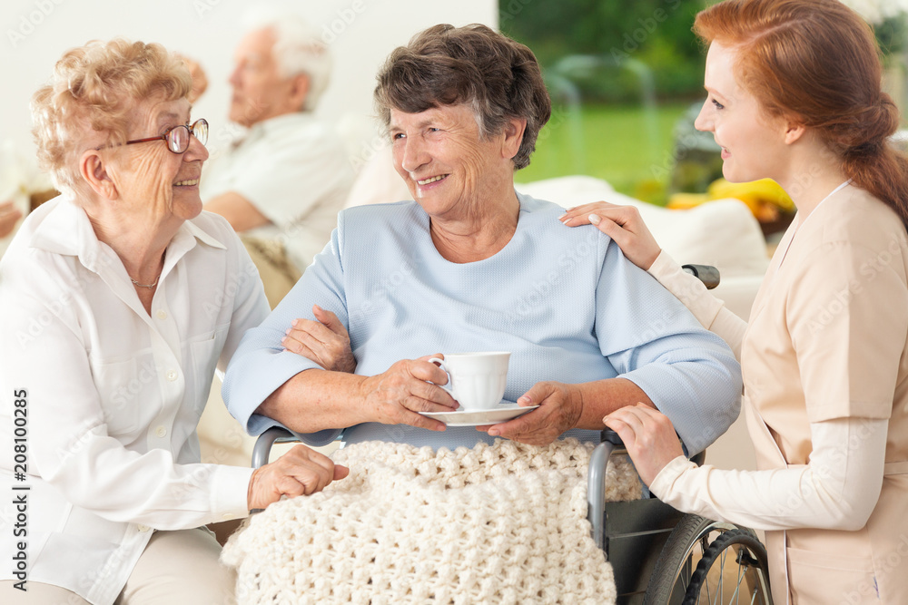 Wall mural smiling paralysed senior woman between happy friend and nurse