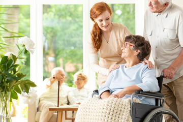 Caregiver and senior man supporting disabled elderly woman in the nursing house