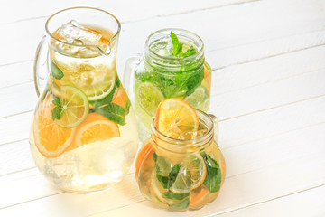 Glass jug and glasses with fresh lemonade stand on white wooden rustic boards in bright light. Copy space