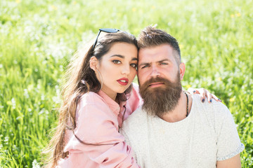 Man with beard and woman sits on grass spring day. Spring leisure concept. Couple in love spend time outdoors and hugs. Couple on happy dreamy faces sitting at meadow, nature on background