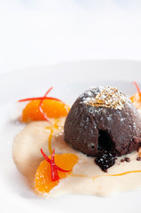 French dessert. Chocolate fondant lava cake with vanilla sauce, citrus and gold leaf on white plate close up view