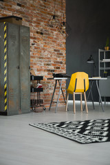 Yellow chair at desk in industrial workspace interior with cabinet against brick wall. Real photo