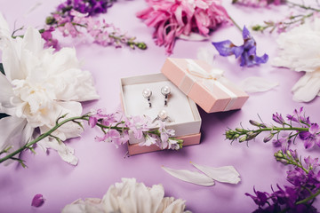 Set of pearl jewellery in gift box with fresh flowers. Silver earrings and ring as a present on purple background.