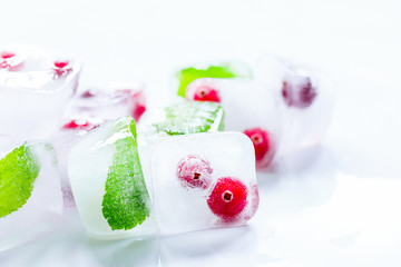 Obraz na płótnie Canvas Ice cubes with berries and mint for summer drink on white backgr