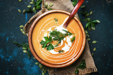 Creamy pumpkin soup with herbs and seeds in wooden bowl, rustic style, black background, top view