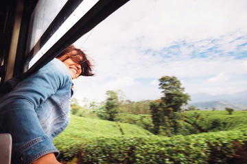 Happy woman looks out from train window during traveling on most picturesque train road in Sri Lanka