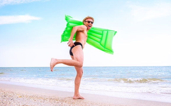 Crazy happy man with swimming mattress runs in the sea
