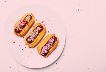 Eclairs cakes with chocolate icing and colorful sugar powder, white background, top view