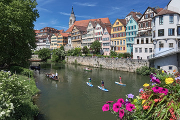 Picturesque view of historical center of Tubingen, Germany. Unidentified people ride along the Neckar river on the traditional punt boats and standup paddle boards, and have a rest at the embankment.